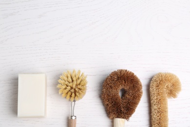 Photo of Cleaning brushes and soap bar on white wooden table, flat lay with space for text. Dish washing supplies