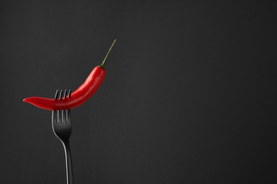 Photo of Fork with chili pepper on black background, space for text