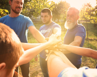 Image of Group of volunteers joining hands together outdoors on sunny day