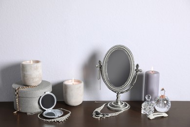 Small mirror, perfume bottles and jewelry on wooden table near light wall