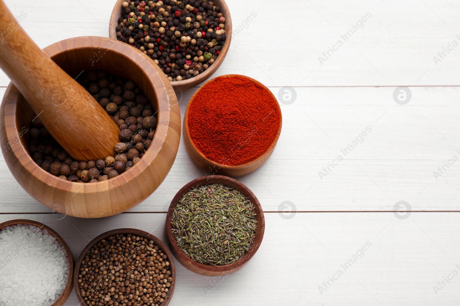 Photo of Mortar with pestle and different spices on white wooden table, flat lay. Space for text