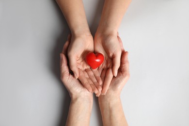 Photo of Young and elderly women holding red heart on light grey background, top view