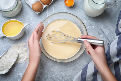 Photo of Woman preparing batter for thin pancakes at grey table, top view