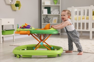 Photo of Cute baby making first steps with toy walker at home