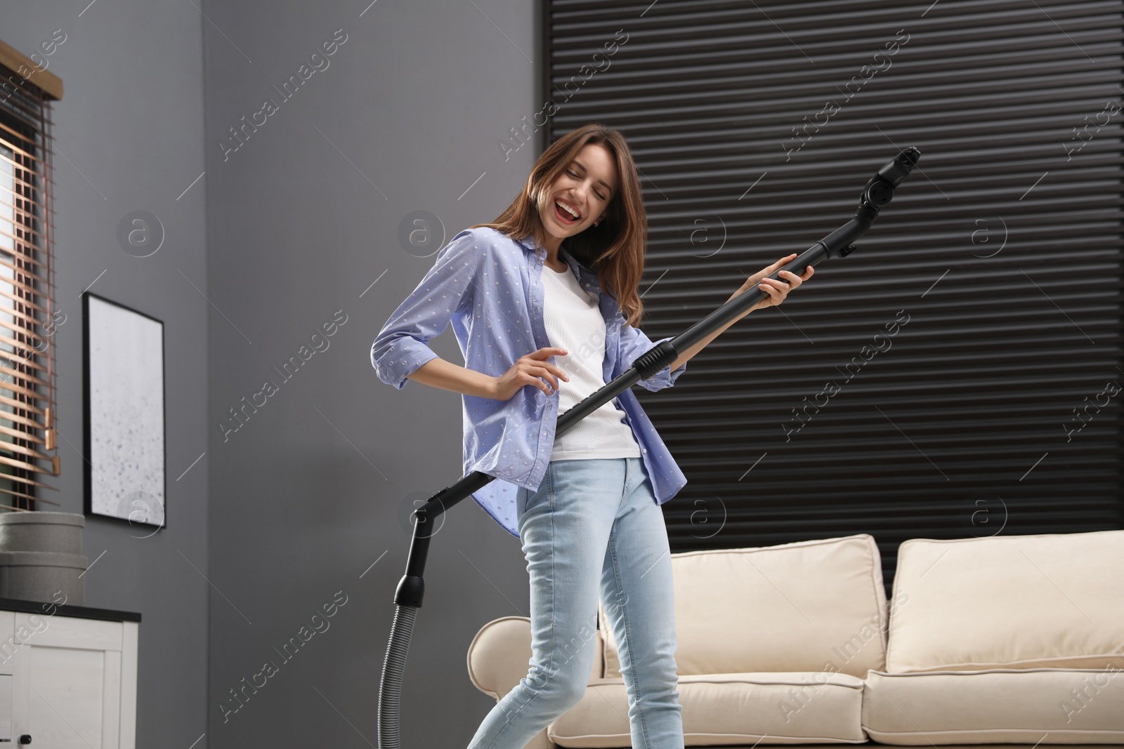 Photo of Young woman having fun while vacuuming at home