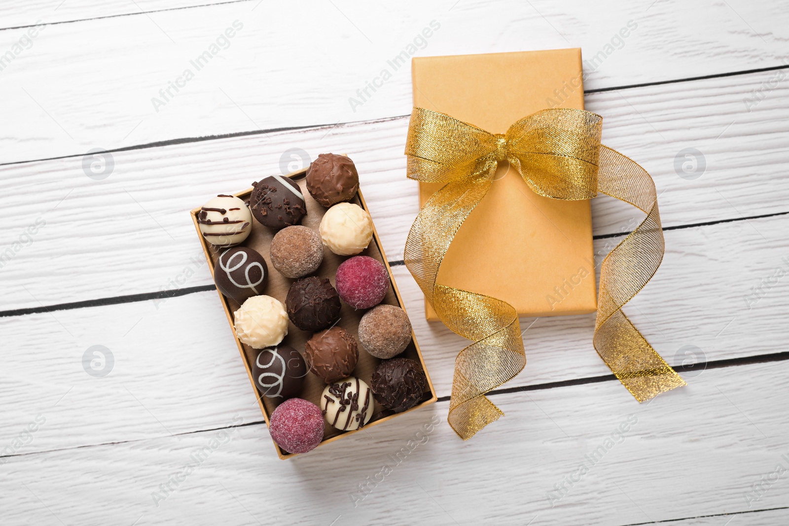 Photo of Open box with delicious chocolate candies on white wooden table, top view