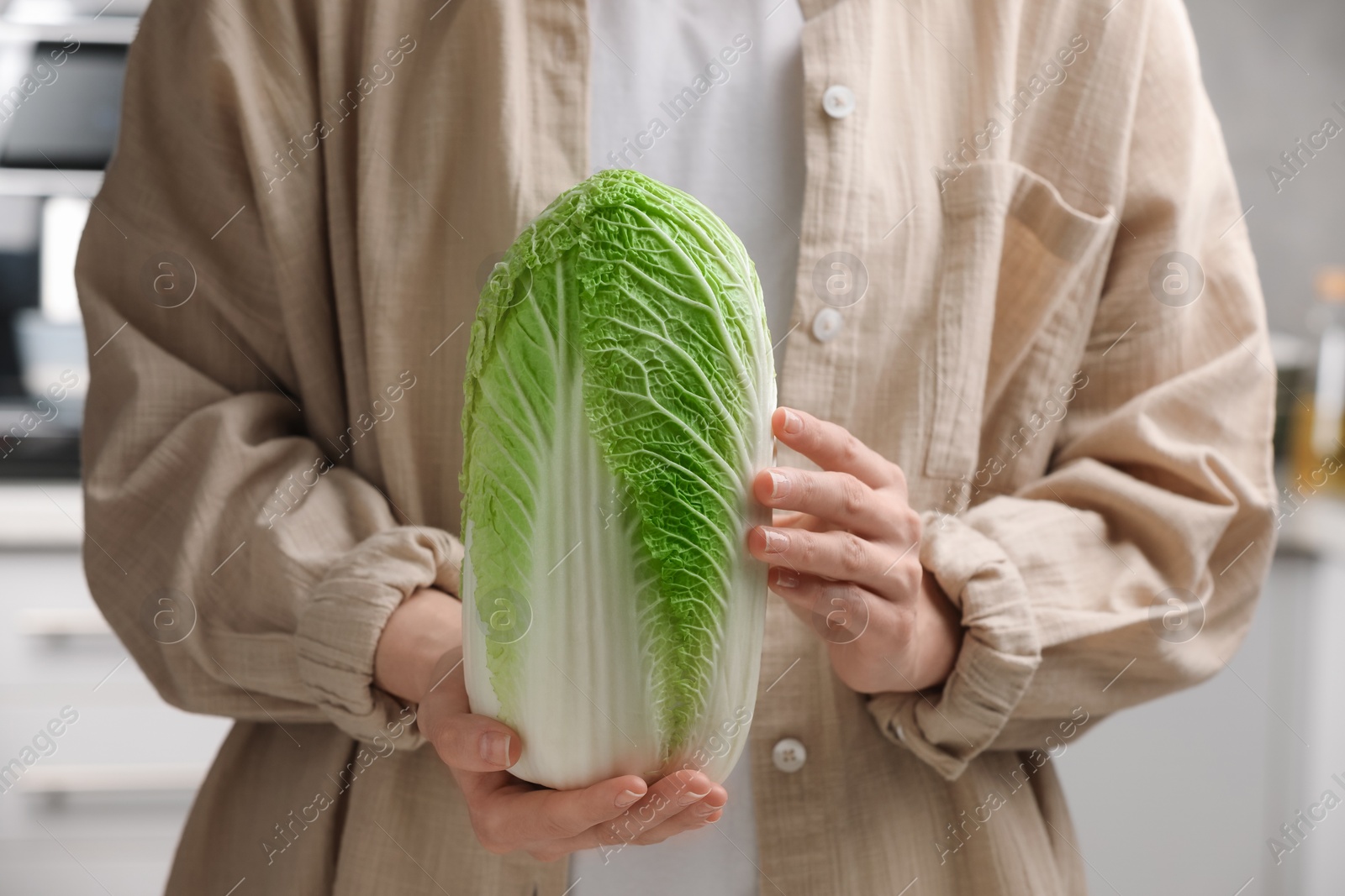 Photo of Woman holding fresh chinese cabbage in kitchen, closeup