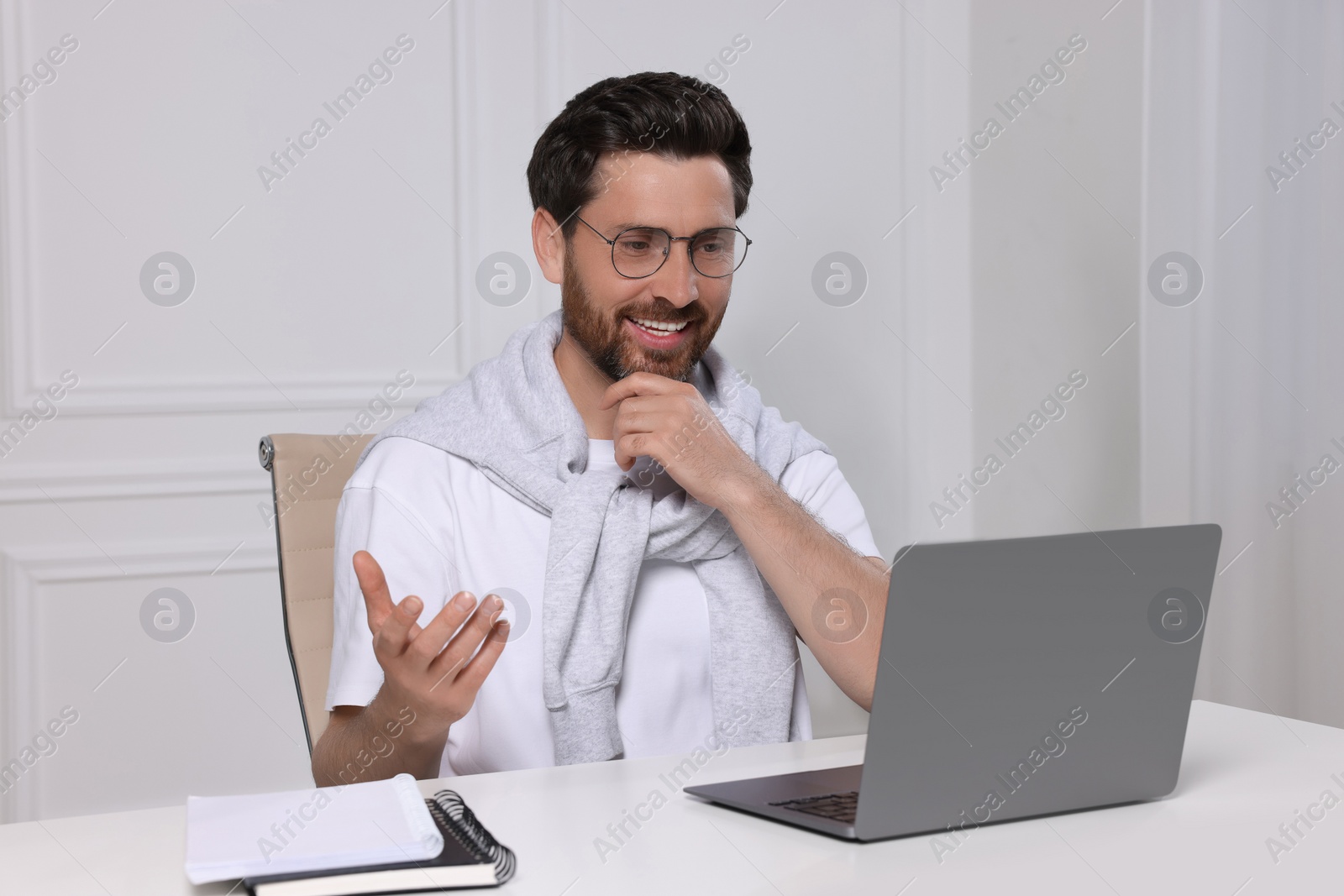 Photo of Man having video chat via laptop at white table indoors