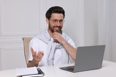 Photo of Man having video chat via laptop at white table indoors