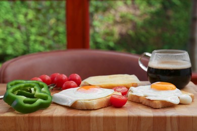 Photo of Tasty toasts with fried egg, cheese and vegetables on wooden board indoors