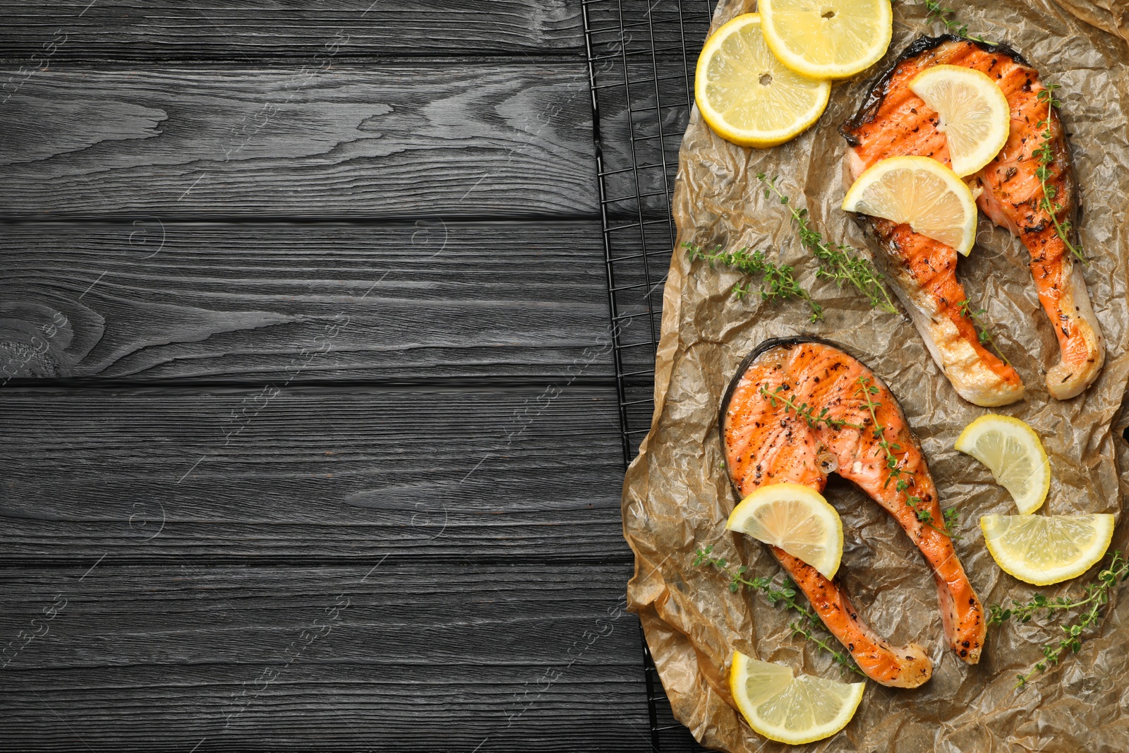 Photo of Tasty grilled salmon steaks and ingredients on black wooden table, top view. Space for text