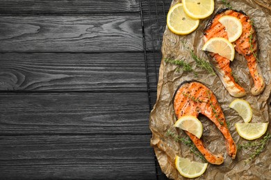 Tasty grilled salmon steaks and ingredients on black wooden table, top view. Space for text