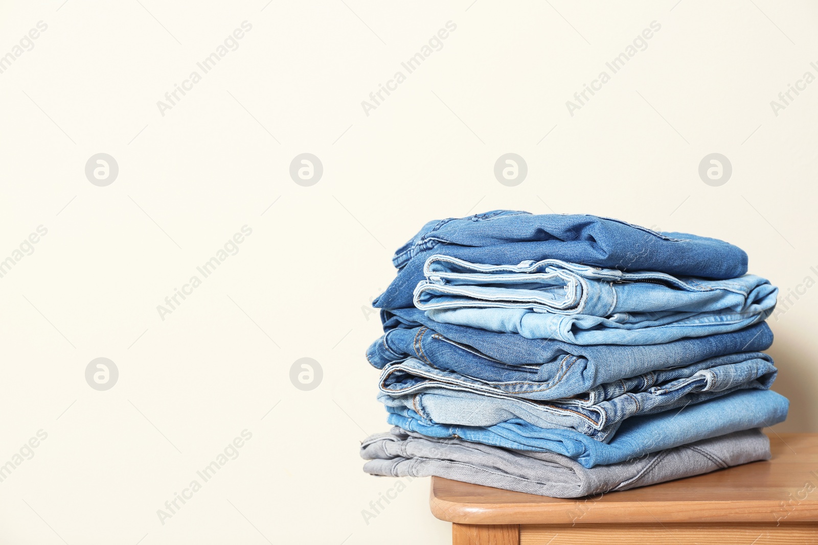 Photo of Stack of different jeans on table against light background. Space for text