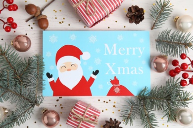 Flat lay composition with Christmas card and festive decor on white wooden background