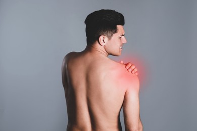 Man suffering from shoulder pain on grey background