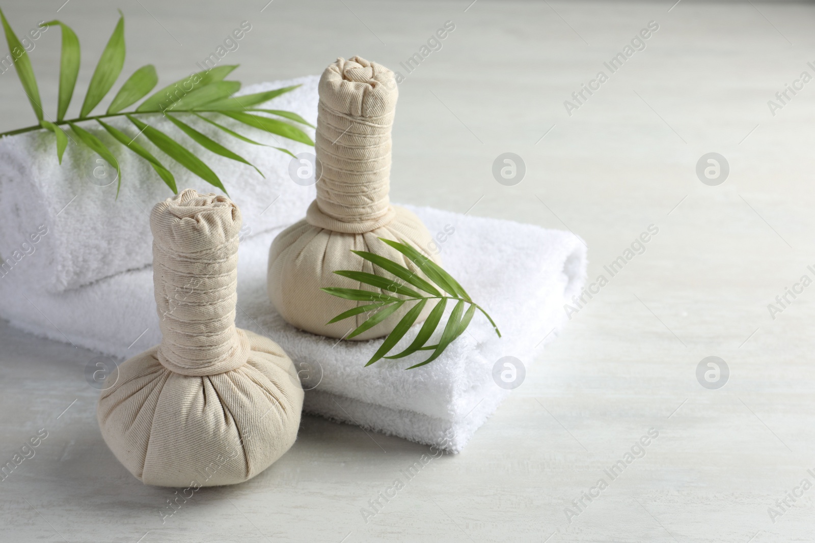 Photo of Spa composition. Herbal bags, towels and palm leaves on light table, space for text