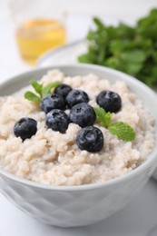 Photo of Delicious barley porridge with blueberries and mint in bowl on white table, closeup