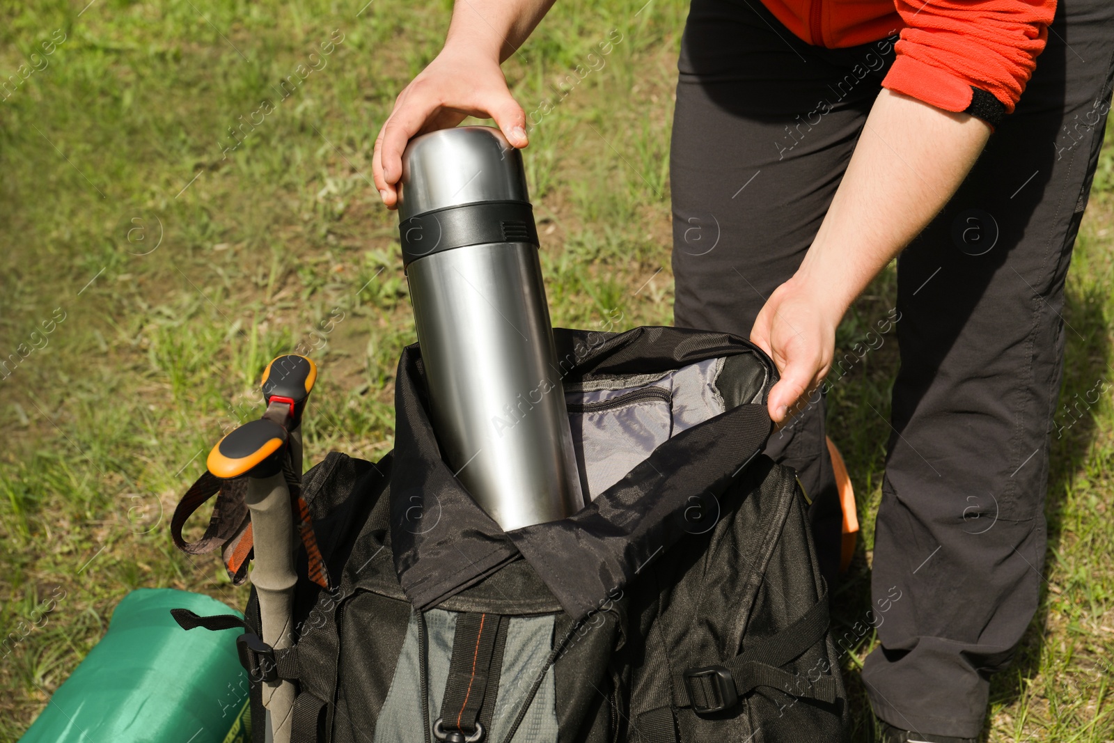 Photo of Hiker putting thermos into backpack outdoors, closeup