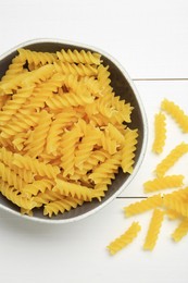 Photo of Raw fusilli pasta in bowl on white wooden table, top view