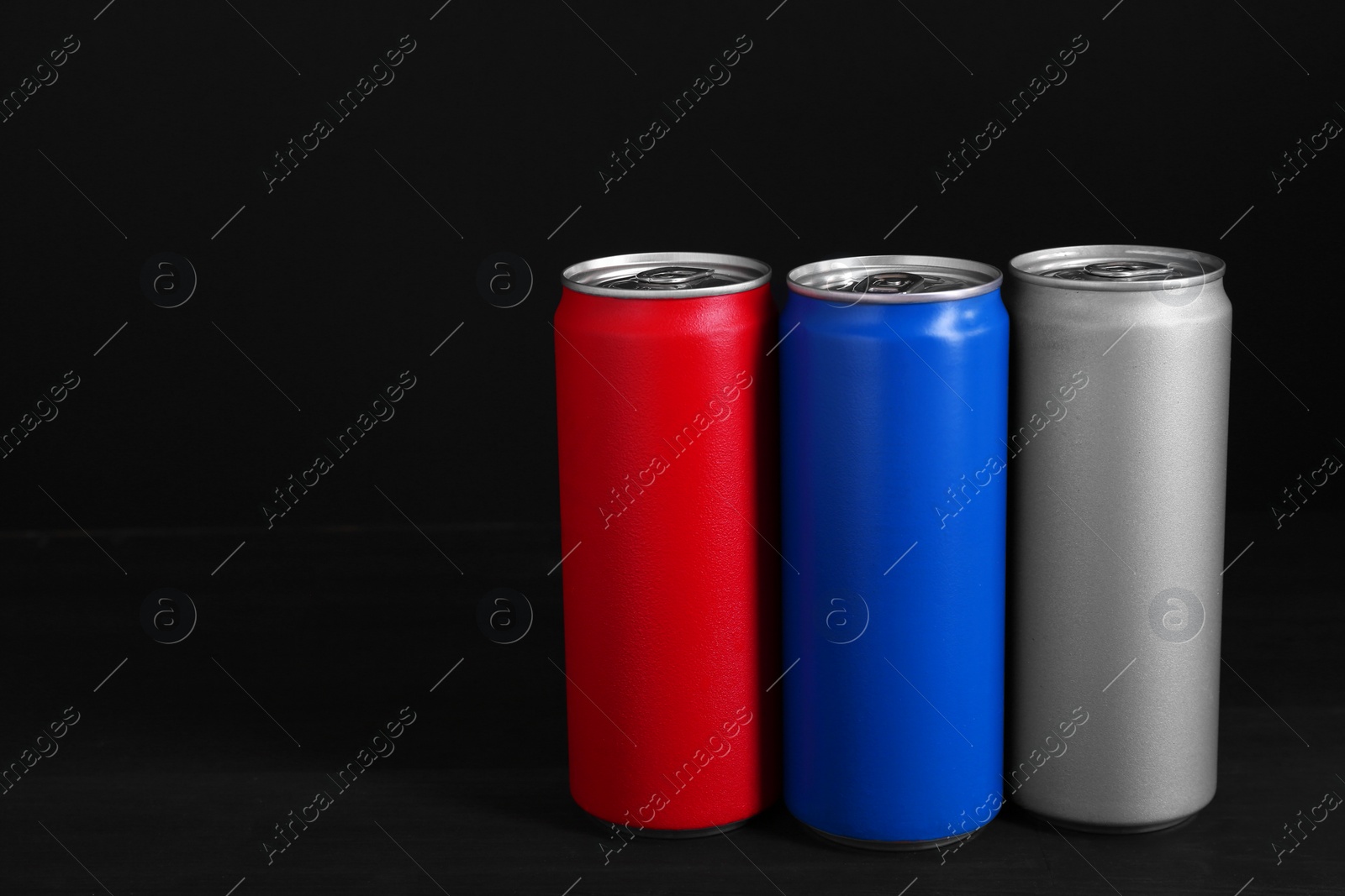 Photo of Energy drinks in colorful cans on black wooden table, space for text