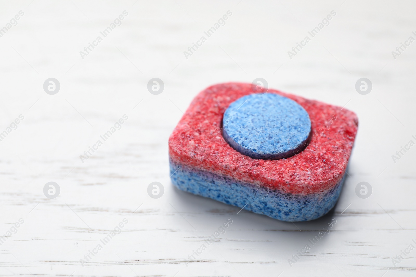 Photo of Dishwasher detergent tablet on white wooden table, closeup. Space for text