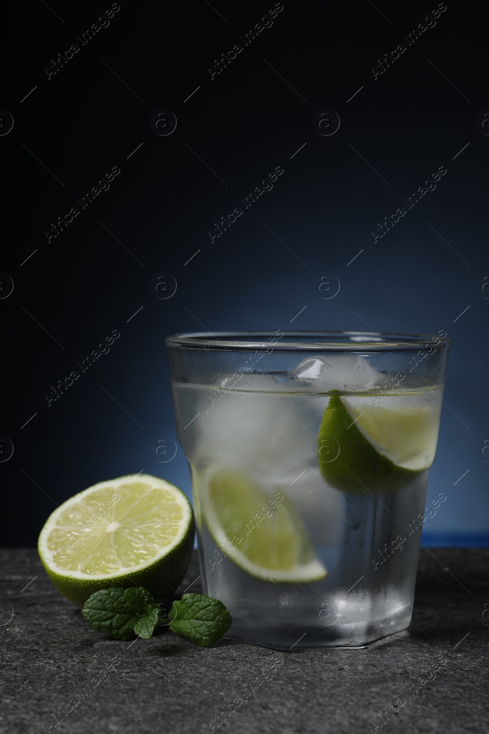 Photo of Glass of vodka with lime slices, mint and ice on grey table