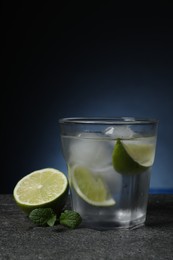 Photo of Glass of vodka with lime slices, mint and ice on grey table