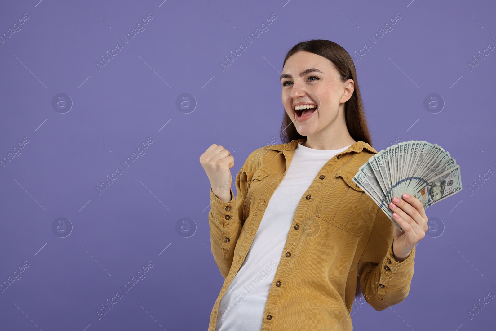 Photo of Excited woman with dollar banknotes on purple background, space for text