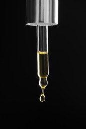 Photo of Dripping tincture from pipette on black background, closeup