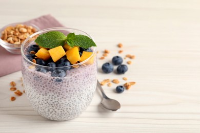 Photo of Delicious chia pudding with blueberries, mango and mint on white wooden table, space for text