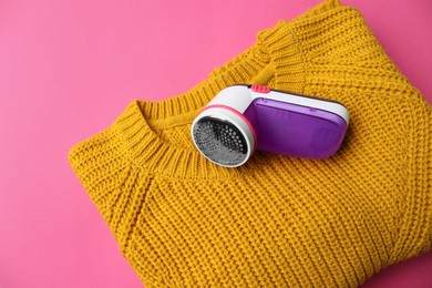 Modern fabric shaver and woolen sweater on pink background, top view