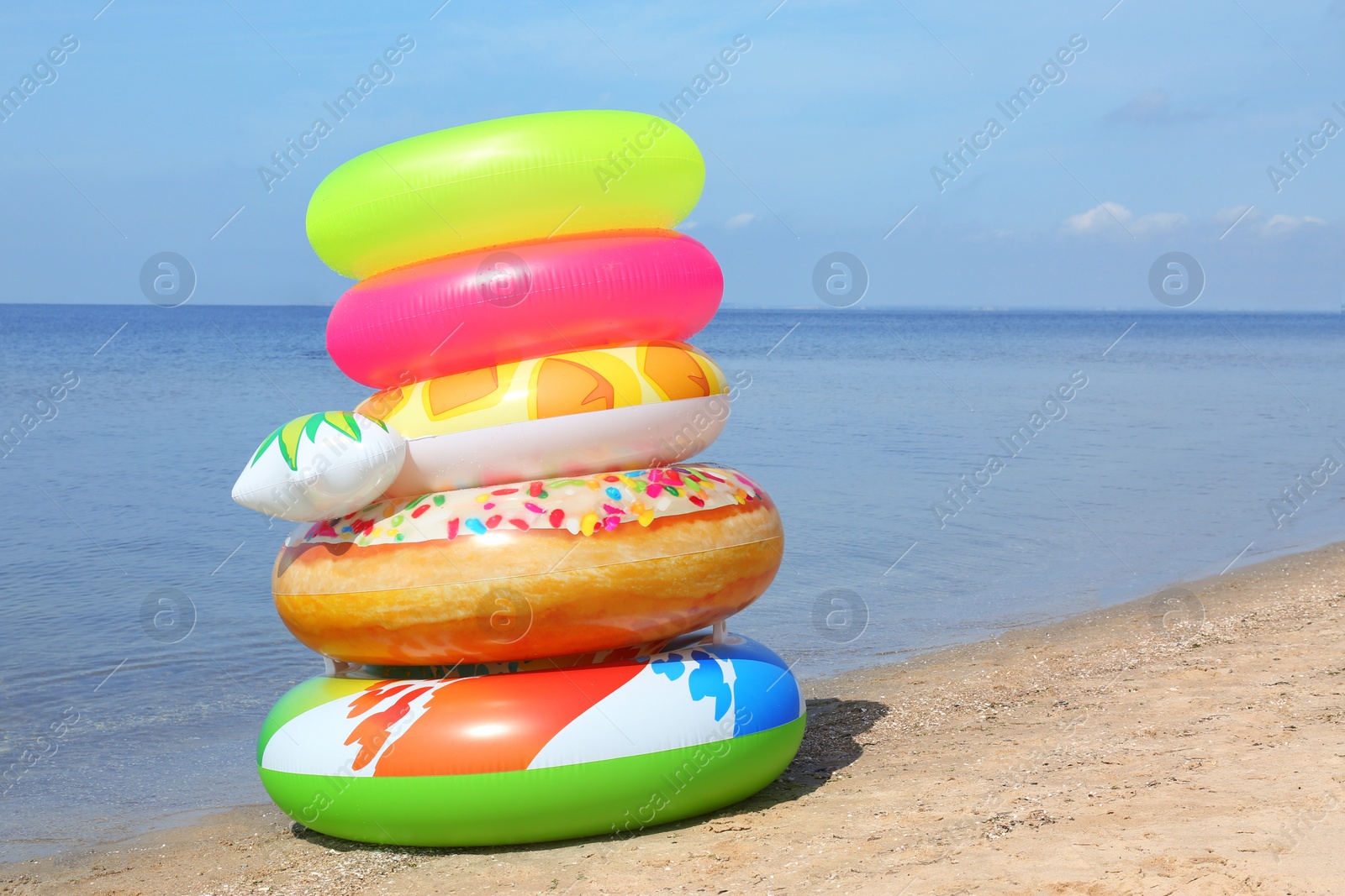 Photo of Stack of different bright inflatable rings on sandy beach near sea. Space for text