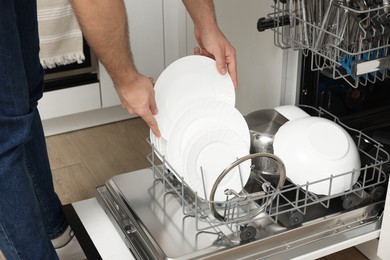 Photo of Man loading dishwasher with plates indoors, closeup