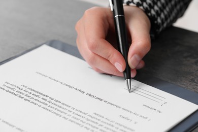 Photo of Woman signing document at dark table, closeup