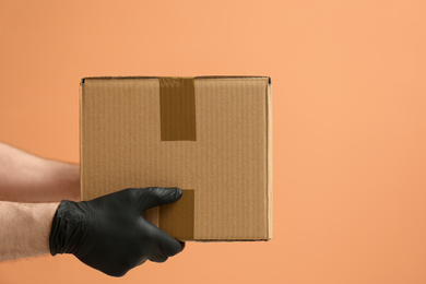 Photo of Courier holding cardboard box on orange background, closeup. Parcel delivery