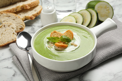 Photo of Tasty homemade zucchini cream soup served on marble table