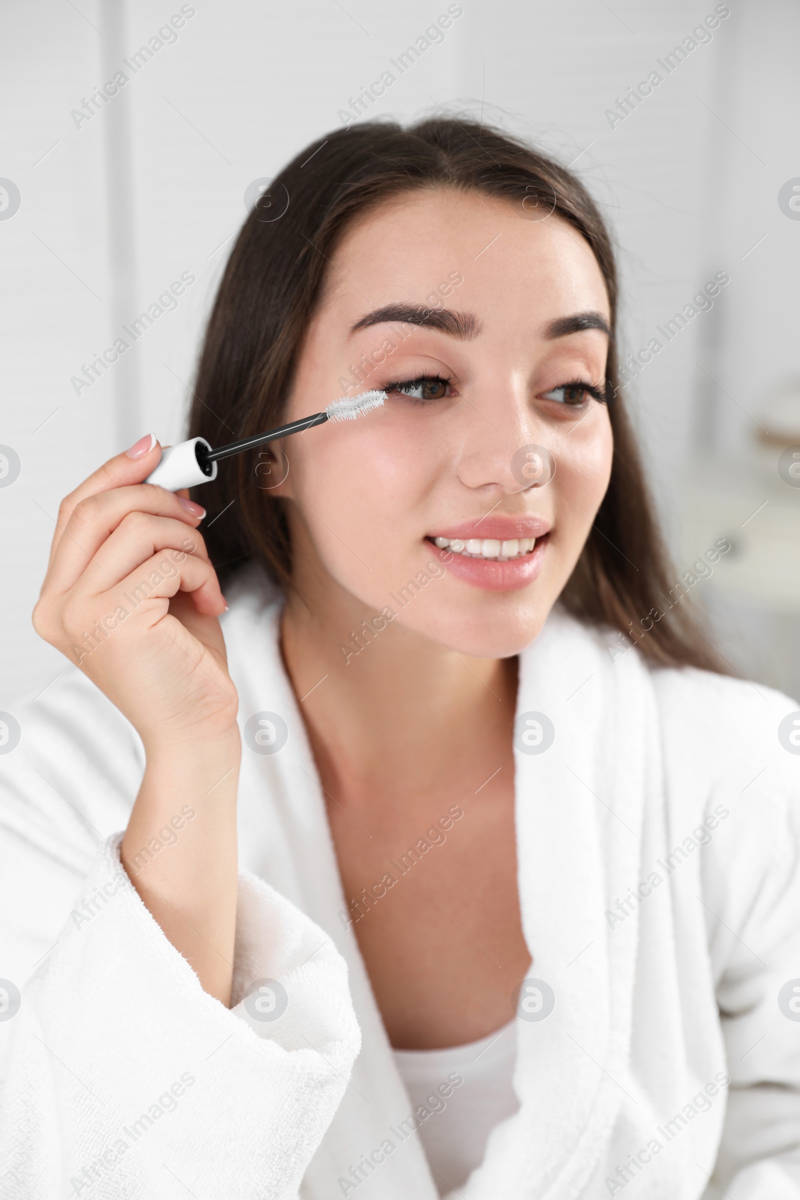 Photo of Attractive young woman applying oil onto her eyelashes indoors