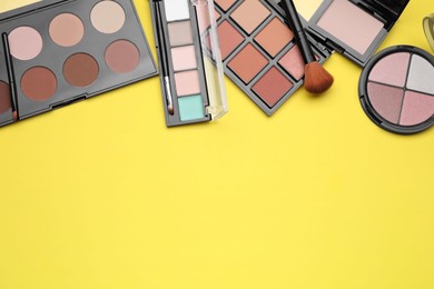 Photo of Different contouring palettes and brushes on yellow background, flat lay with space for text. Professional cosmetic product
