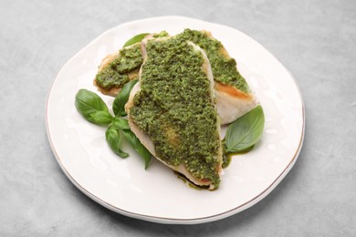 Delicious chicken breasts with pesto sauce and basil on light gray table, closeup