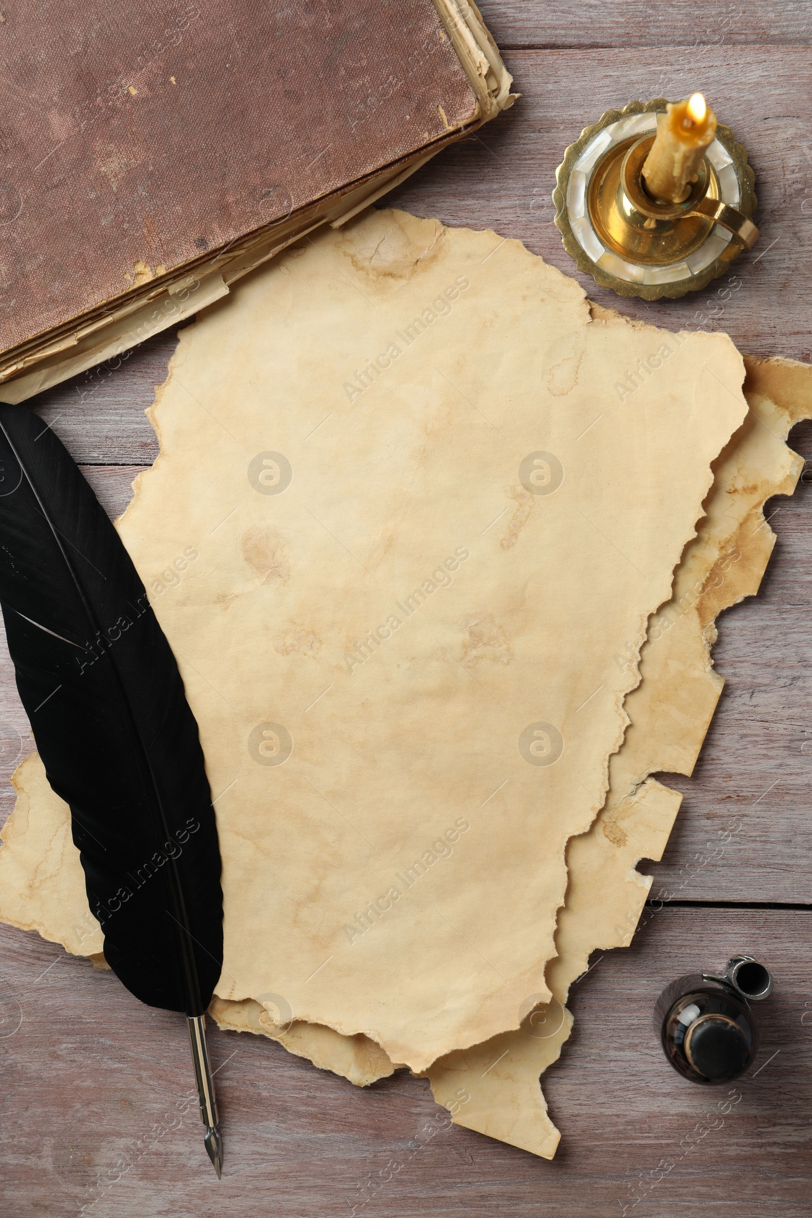 Photo of Sheet of old parchment paper, black feather, inkwell, vintage book and candle on wooden table, flat lay