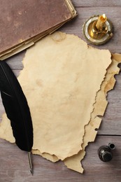 Sheet of old parchment paper, black feather, inkwell, vintage book and candle on wooden table, flat lay