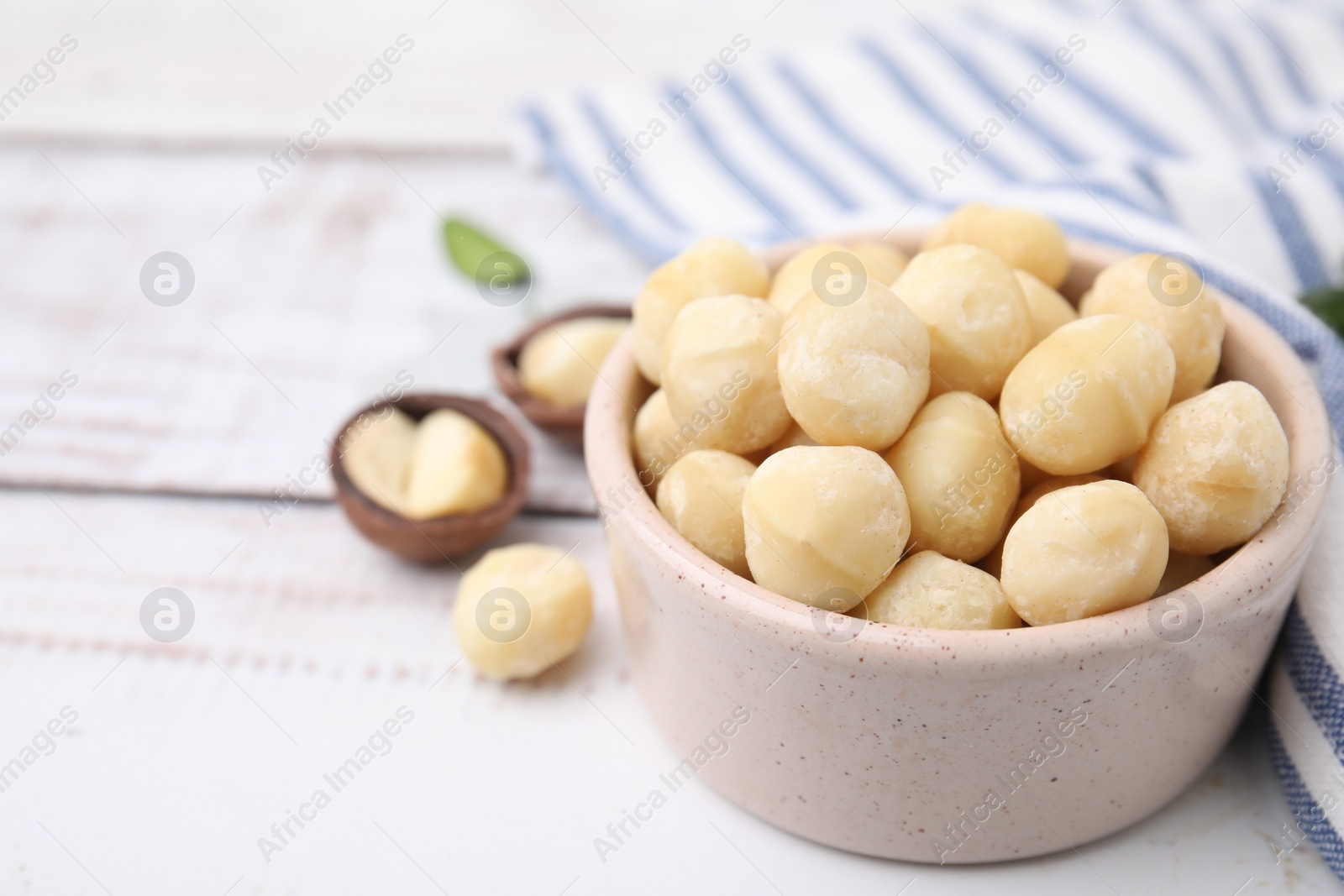 Photo of Tasty peeled Macadamia nuts in bowl on light table, closeup. Space for text