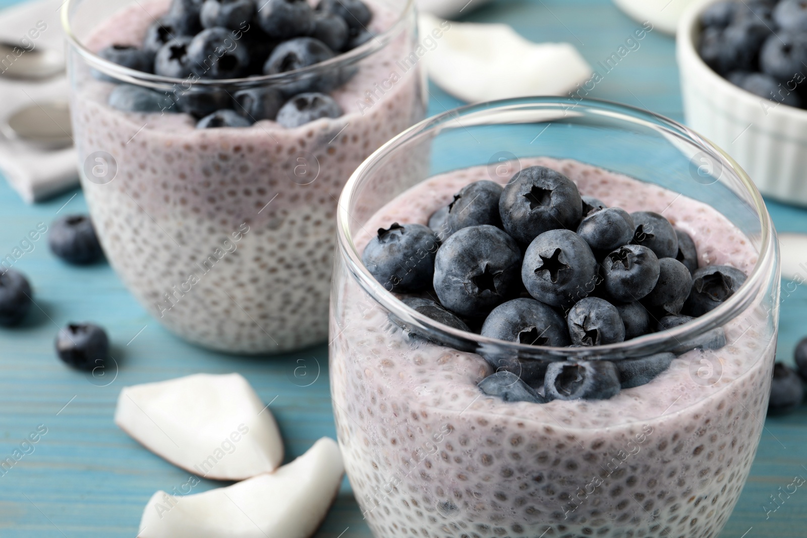 Photo of Delicious chia pudding with blueberries in glass on light blue table, closeup