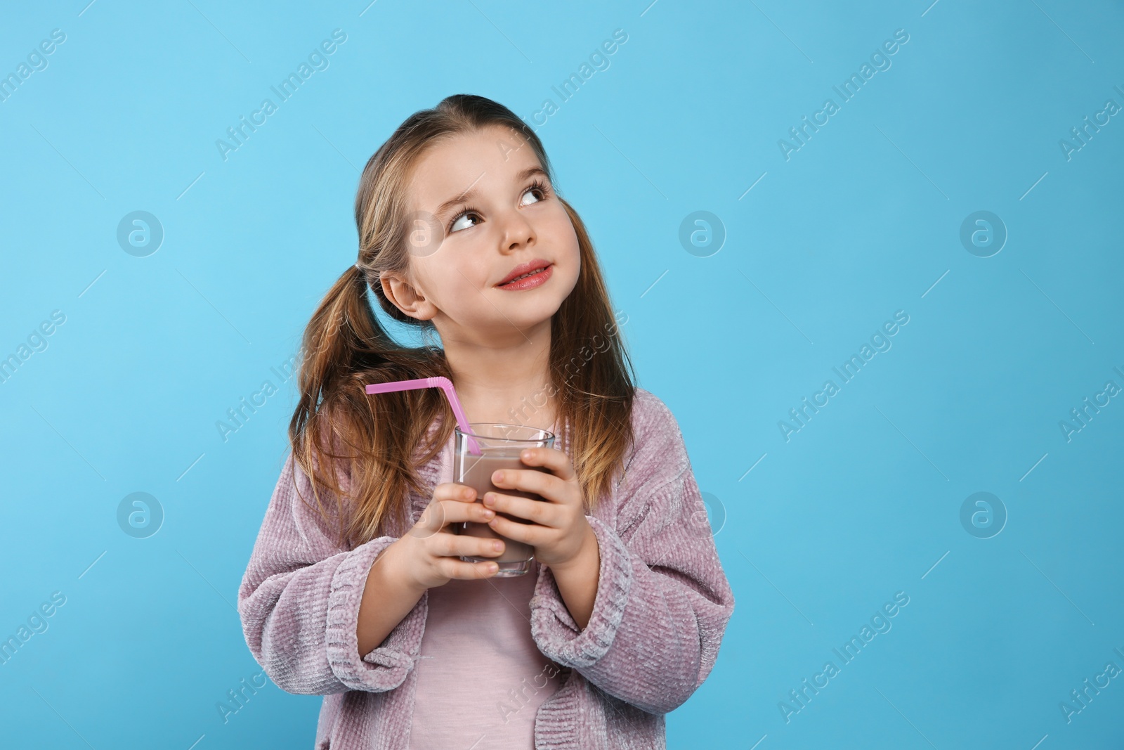 Photo of Cute little child with glass of tasty chocolate milk on light blue background