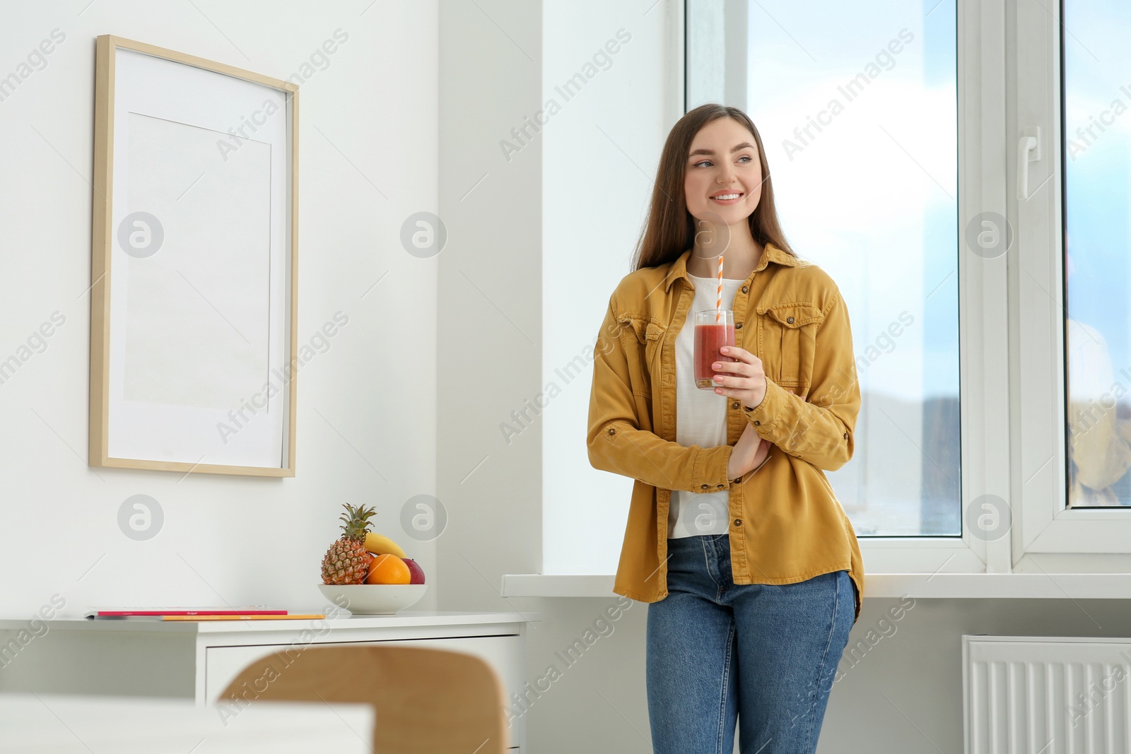 Photo of Beautiful young woman with delicious smoothie near window at home. Space for text