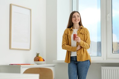 Beautiful young woman with delicious smoothie near window at home. Space for text