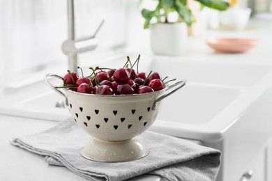 Photo of Fresh ripe cherries with water drops in colander on countertop indoors