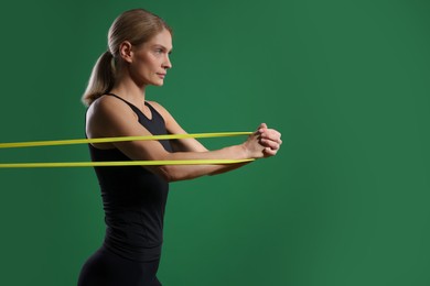 Athletic woman exercising with elastic resistance band on green background. Space for text