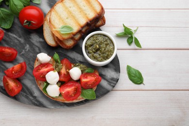 Photo of Delicious Caprese sandwich with mozzarella, tomatoes, basil and pesto sauce on white wooden table, top view