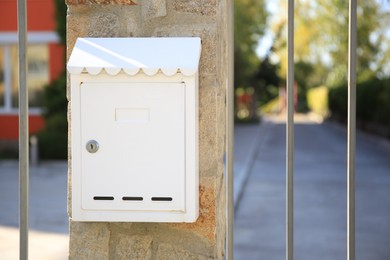 Photo of White metal letter box on stone column near fence outdoors